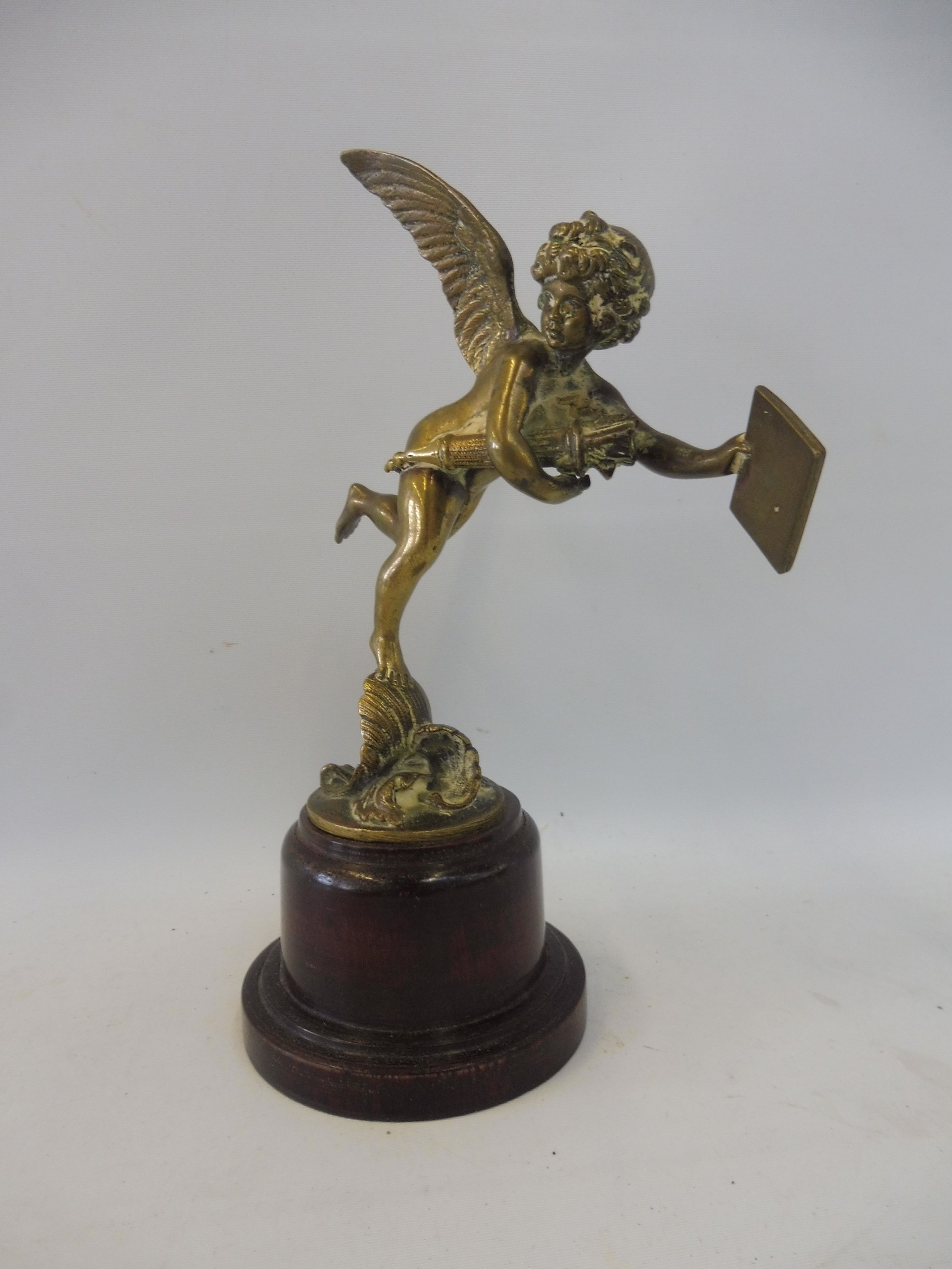 A polished brass accessory mascot in the form of a winged cherub, display base mounted.