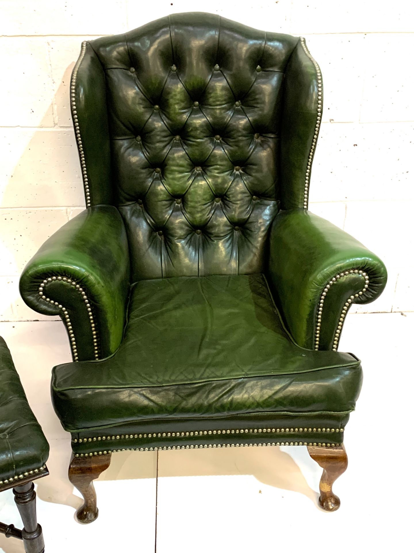 Green brass studded button back leather upholstered wing back armchair with a similar footstool. - Image 3 of 7