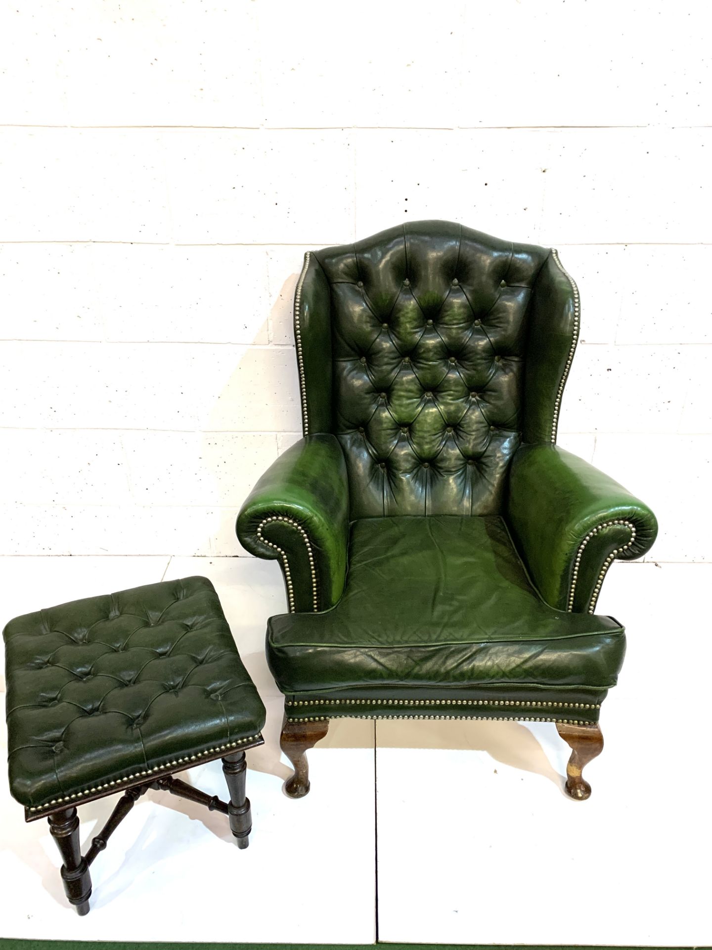 Green brass studded button back leather upholstered wing back armchair with a similar footstool.