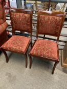 Pair of dining chairs with sabre legs upholstered in dark red and gold floral design.