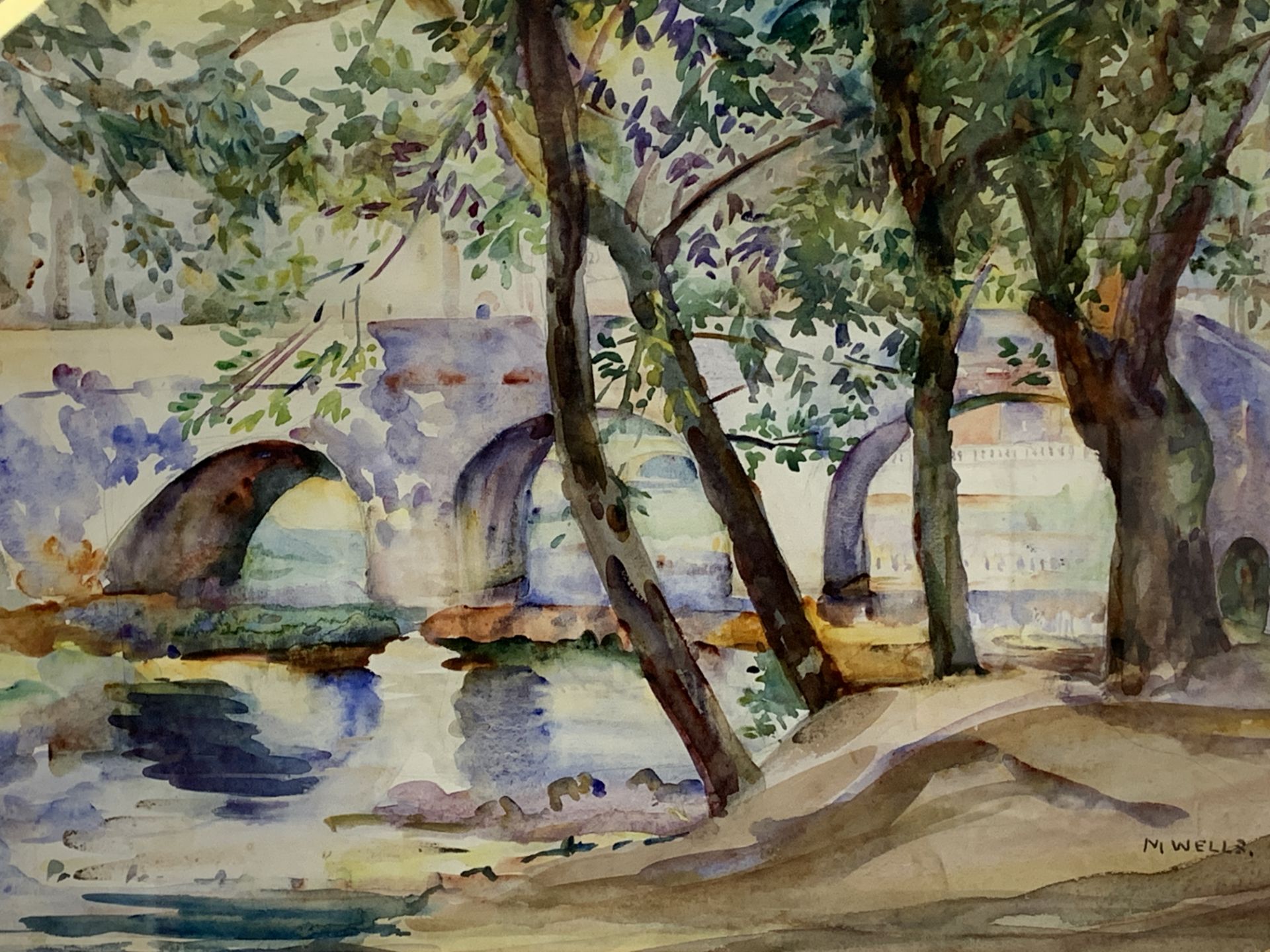 Framed and glazed watercolour of trees by a river and a bridge, signed M Wells