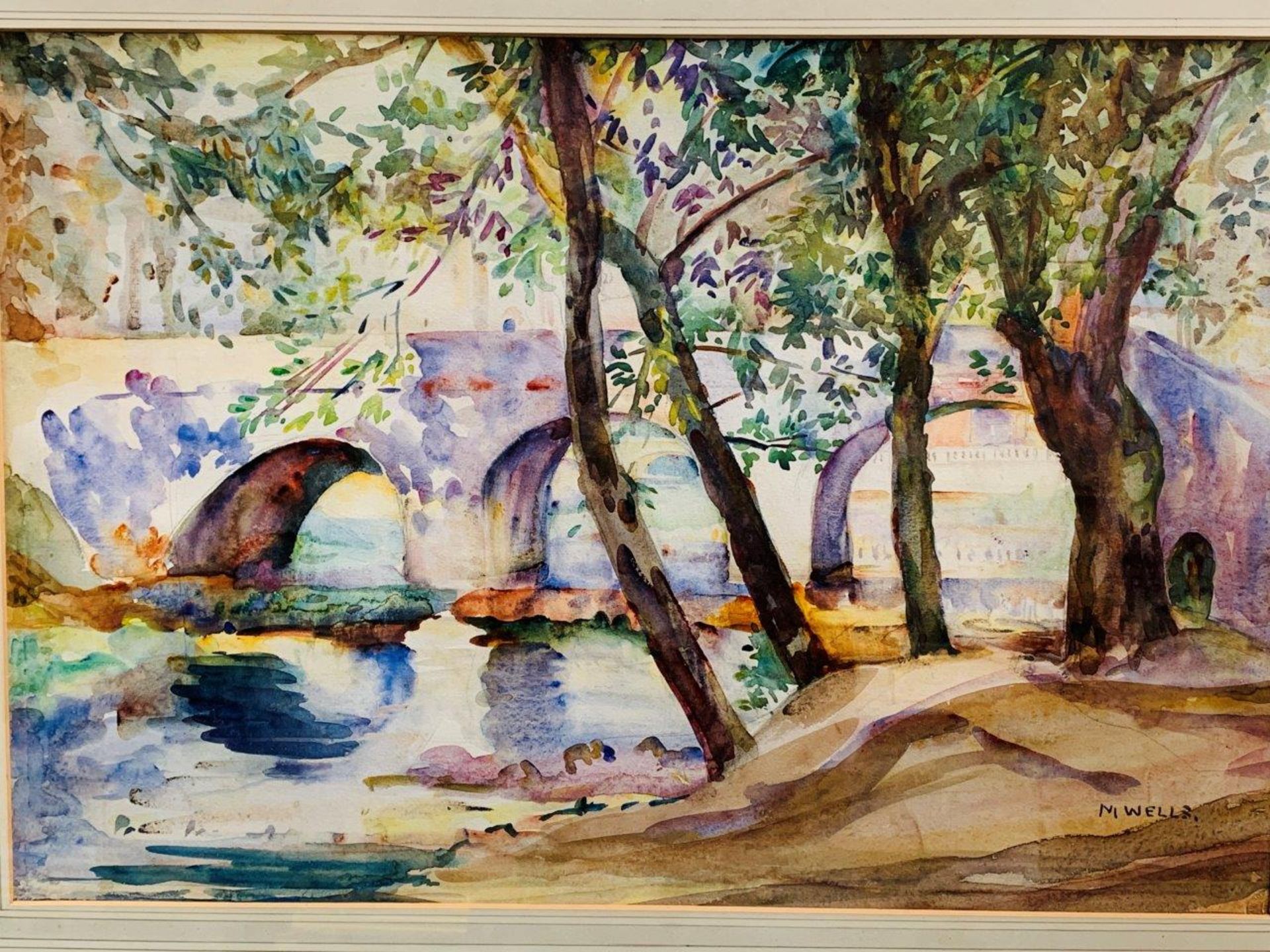 Framed and glazed watercolour of trees by a river and a bridge, signed M. Wells