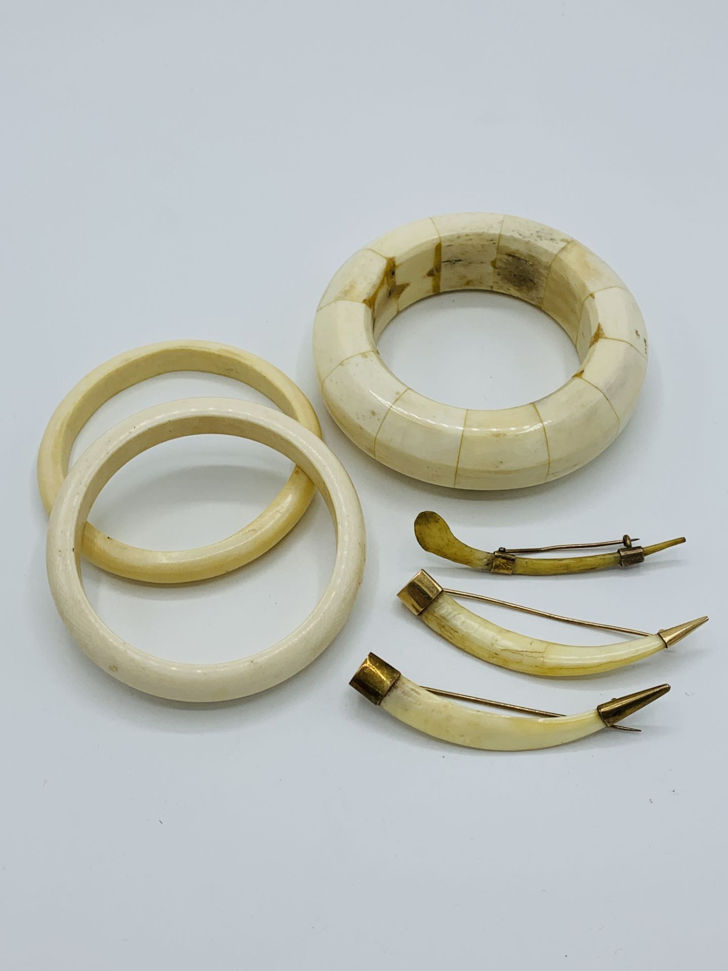 Three bone bangles and 3 yellow metal mounted animals' teeth brooches