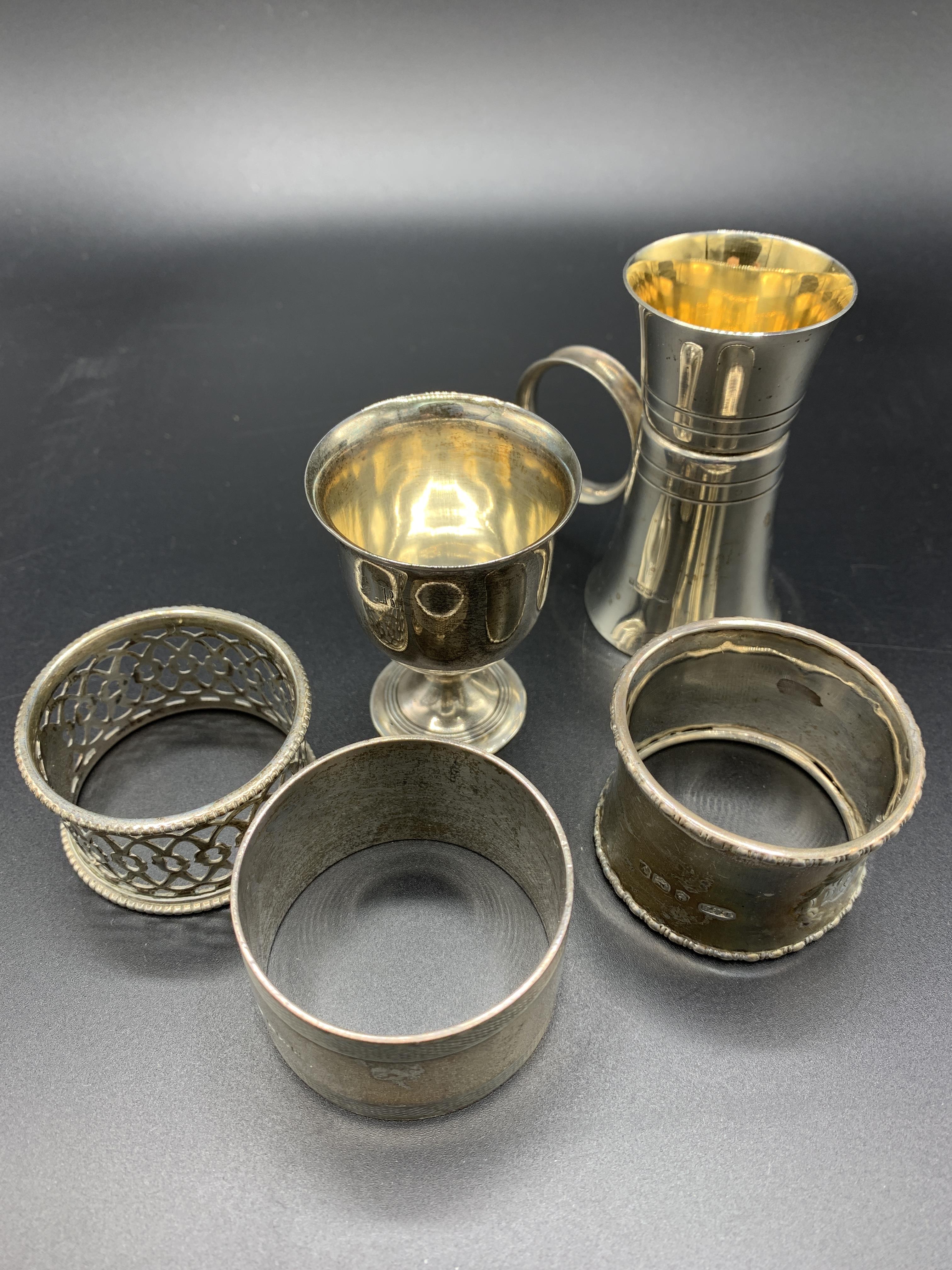 A hallmarked silver and gilt drinks measure, a silver egg cup, and three silver napkin rings