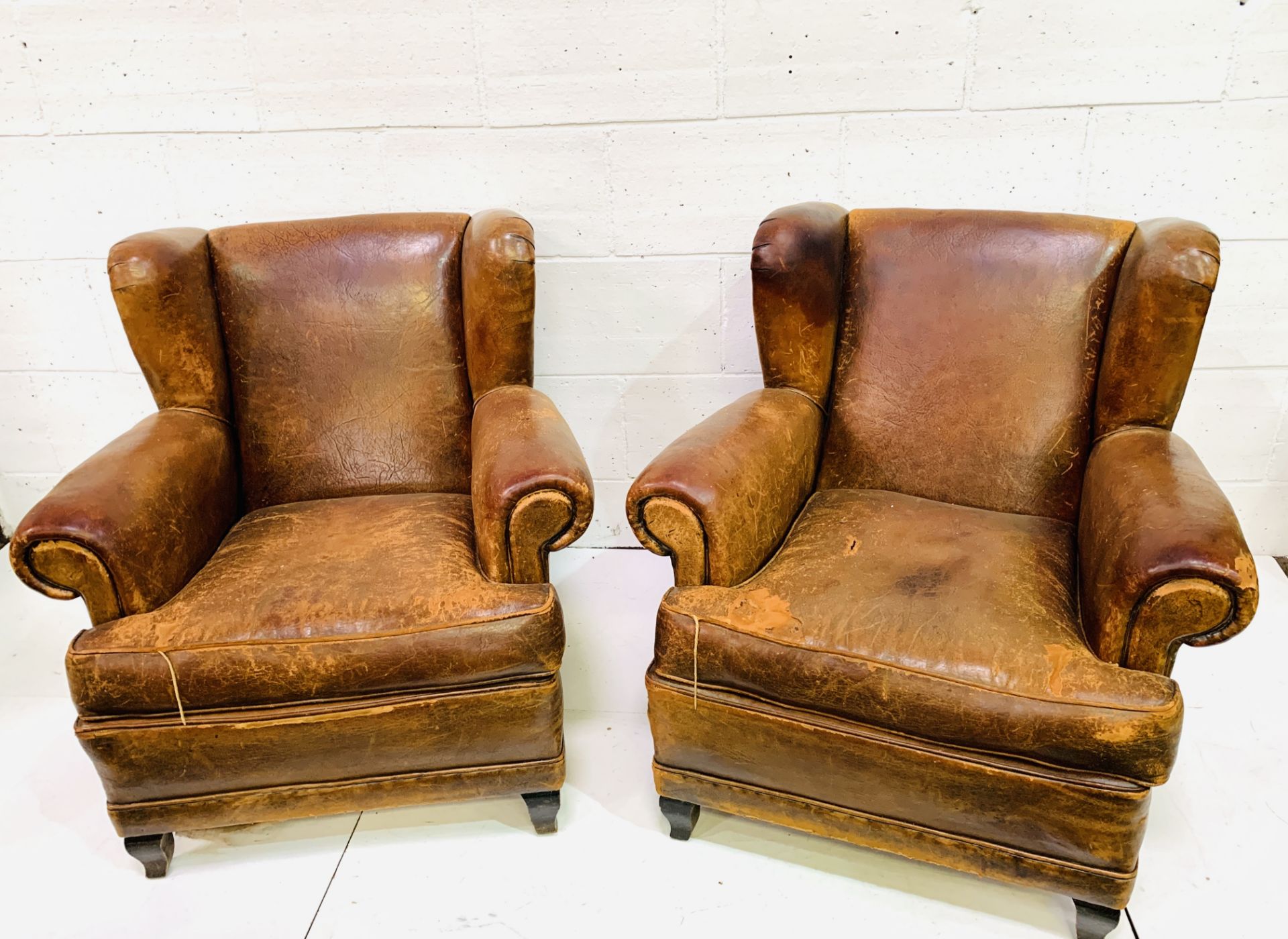 A pair of French brown leather wing back armchairs