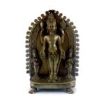 An Indian cast brass figure of a four armed deity, standing within an arch upon a lotus leaf flanked