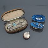Sewing étuis and a pincushion: A white metal sewing set in a fitted oval wooden case, the exterior l