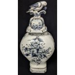 A Delft blue and white vase depicting a man within a landscape scene, the lid in the form of a bird,