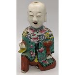 A 19th century Chinese famille rose porcelain laughing boy holding a ruyi in one hand and a fruit in