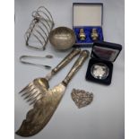 A collection of silver tableware to include a silver toast rack, two silver peppers, silver tongs,