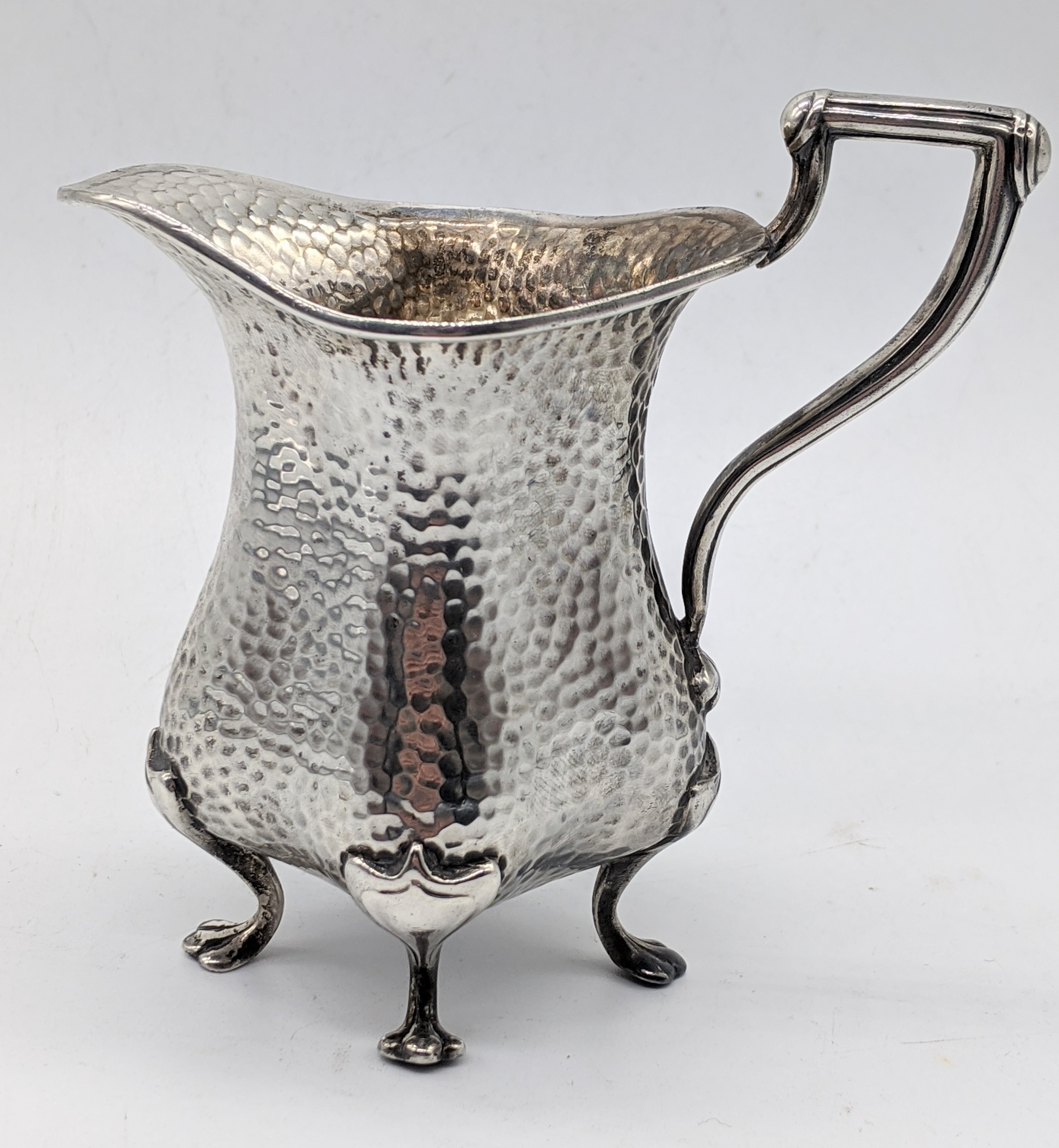 An early 20th century Arts and Crafts silver jug, planished finish, raised on four paw feet,