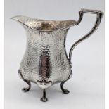 An early 20th century Arts and Crafts silver jug, planished finish, raised on four paw feet,
