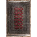 A large Pakistani handmade rug, central geometric design on a red ground, signed, 255cm x 157cm