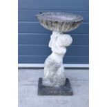 A vintage garden statue in the form of a cherub bird bath on a base, 64cm tall made from