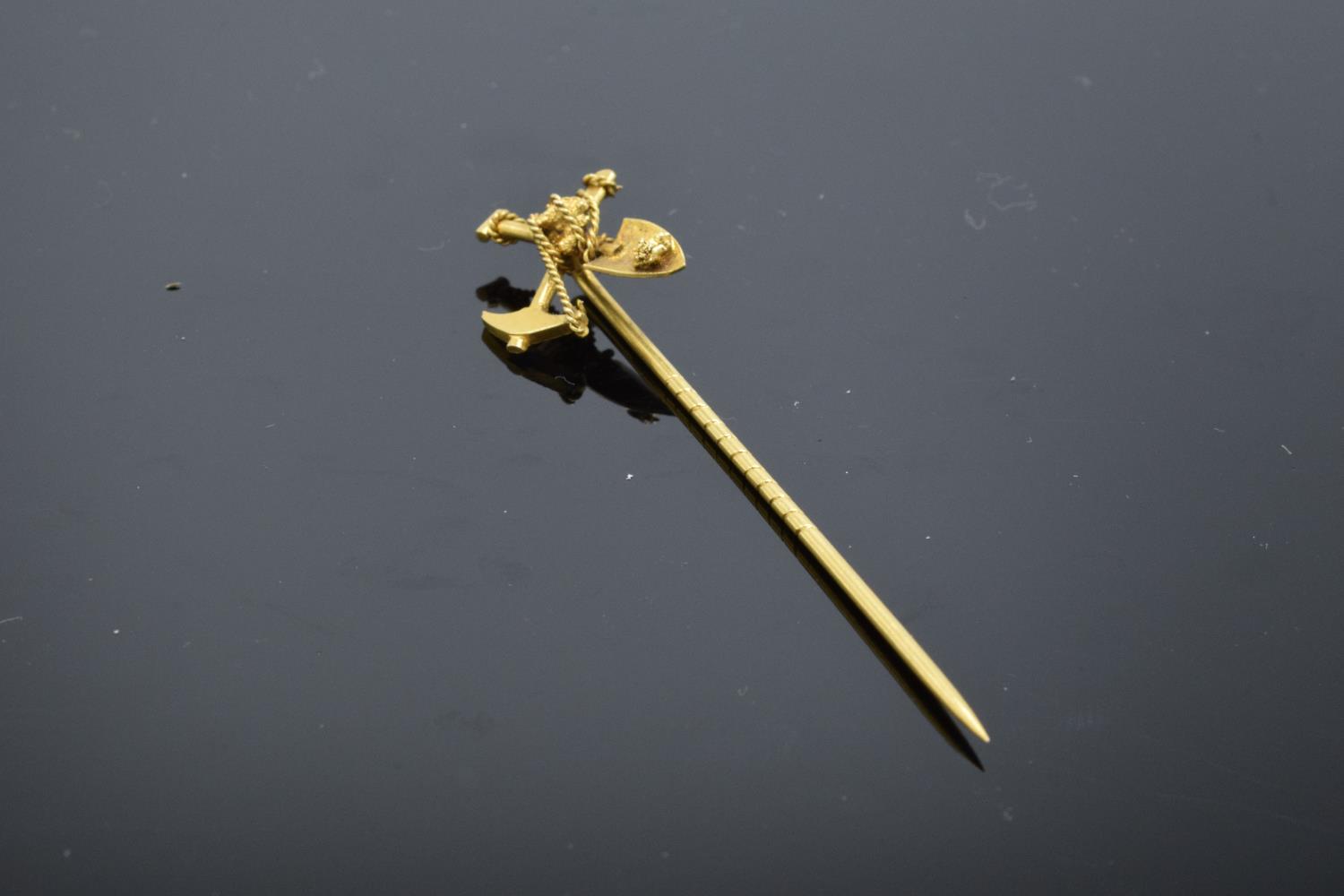 A 9ct gold stick pin in the form of a miner's shovel and pick axe. Tests as 9ct gold. 2.1 grams. 6.5
