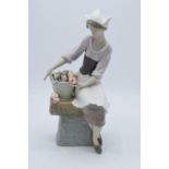 Lladro figurine of a Dutch Girl sat with a basket of flowers. 26cm tall. In good condition with no