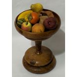 A turned burrwood pedestal bowl with collection of artificial fruit