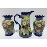 Old Tupton ware jug with pair of matching baluster vases, foliate decorated upon a dark blue ground,