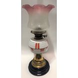 A brass oil lamp with white opaque glass reservoir and cranberry blush etched shade and on black