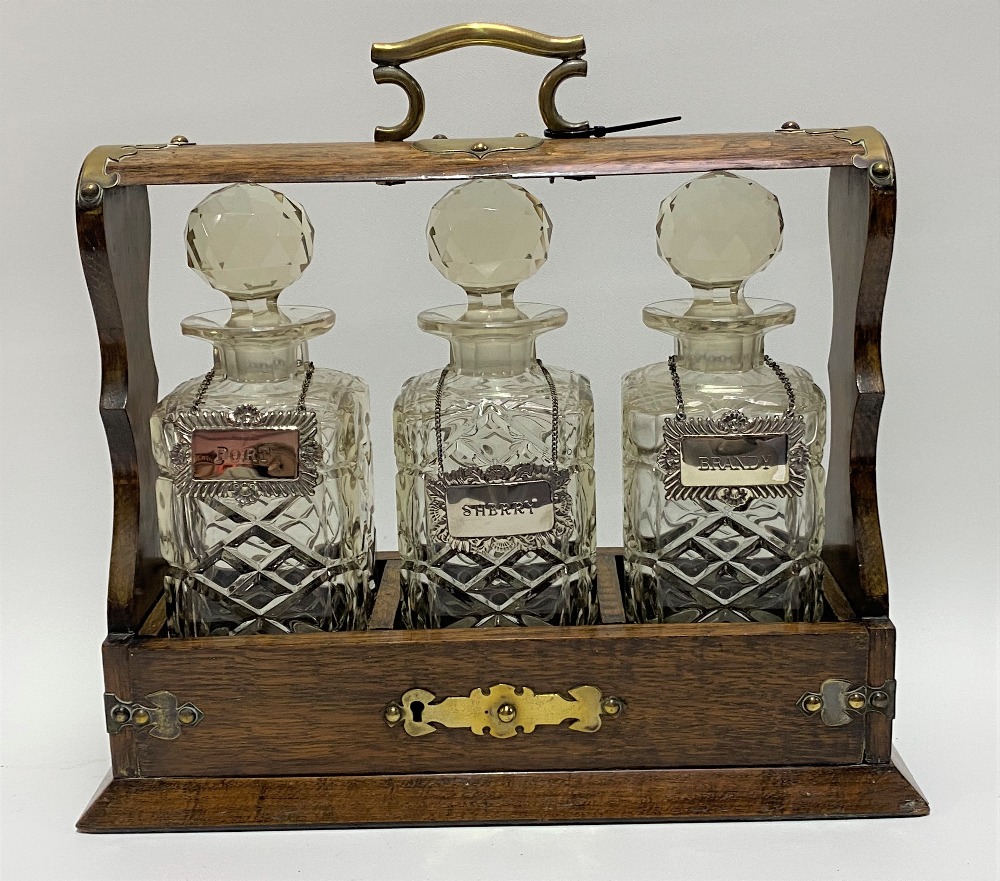 An oak brass bound three-section tantalus enclosing three square section spirit bottles with