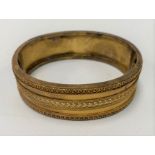 A 19th century yellow metal bangle, tests 9ct, the front with filigree banded decoration, width 5.