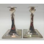 A pair of Edwardian Art Nouveau silver weighted candlesticks of square section flared form,