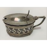 A George V silver hinge-lidded mustard pot of oval section with pierced body, raised on four ball