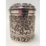 An Indian white metal embossed and chased cylindrical lidded canister, the lid decorated with a
