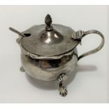 An Edwardian silver hinge-lidded mustard pot with blue glass liner, raised on three outswept feet,