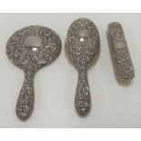 A modern silver three piece foliate scroll embossed and grotesque mask dressing table set comprising