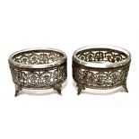 A pair of continental white metal salts with clear glass liners and with pierced foliate scroll