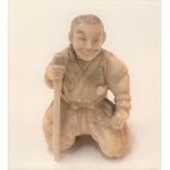 A Meiji period Japanese ivory carved netsuke in the form of a kneeling sage with staff, height