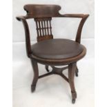 An early 20th century oak swivel office elbow chair with brown rexine upholstered seats upon four