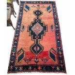 Eastern wool hand knotted rug with central medallion within geometric borders upon a red ground,
