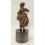 A 19th century bronze sculpture of a woman in 18th century dress holding a wheat sheaf and on