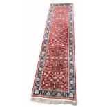 Persian hand knotted wool runner decorated with foliate scrolls and borders upon a red ground,