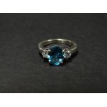 A contemporary 18ct. white gold blue topaz and diamond set three stone ring, the circular oval cut