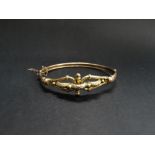 An early 20th century 9ct. gold hinged bangle, the front with loop and foliate cast design,