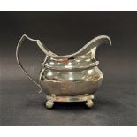 A George III silver oval section milk jug with gadrooned rim raised on four ball feet, maker SW,