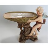 A 19th century Royal Dux Pottery table centrepiece modelled as a cherub holding a shell upon a