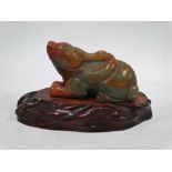 A Chinese green and russet jade carving of a recumbant mythical beast, upon wooden stand, length