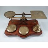 A Victorian brass postal balance scales upon an oak stand with three circular sections for