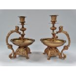A pair of Victorian brass and gilt painted candlesticks, each with strap handles with putti busts