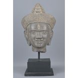 A CAMBODIAN KHMER CARVED STONE HEAD ON PLINTH