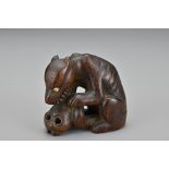A Japanese carved wood netsuke in the form of a wolf with a skull. Signed to base. Meiji period.