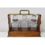 A quality oak & brass three decanter Betjeman tantalus damage to one decanter