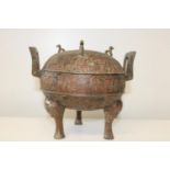 A antique Chinese bronze ritual vessel with tripod legs, and lidded top with open scroll work to the