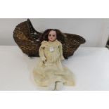 A vintage Armand Marseille bisque headed doll in a period wicker rocking crib crib length 50cm