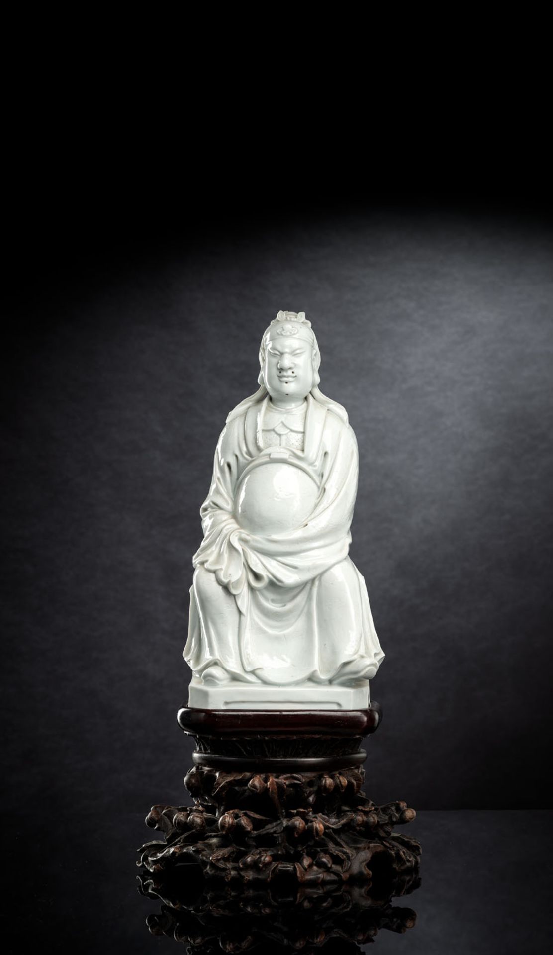 A DEHUA MODEL OF SEATED GUANDI WITH FINELY INCISED ROBE ON CARVED OPENWORK WOOD STAND
