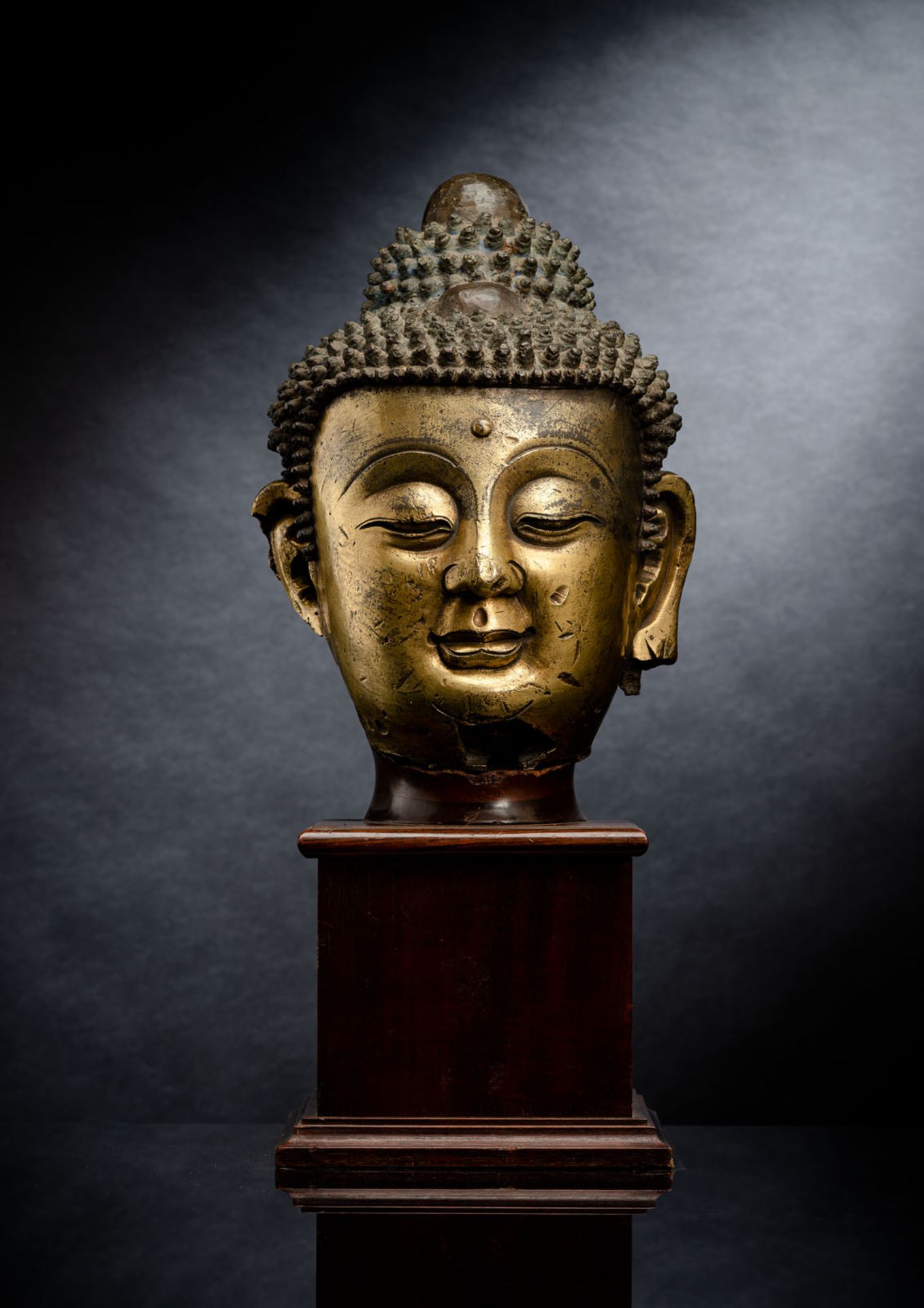 A LARGE GILT-BRONZE HEAD OF BUDDHA ON A WOOD STAND